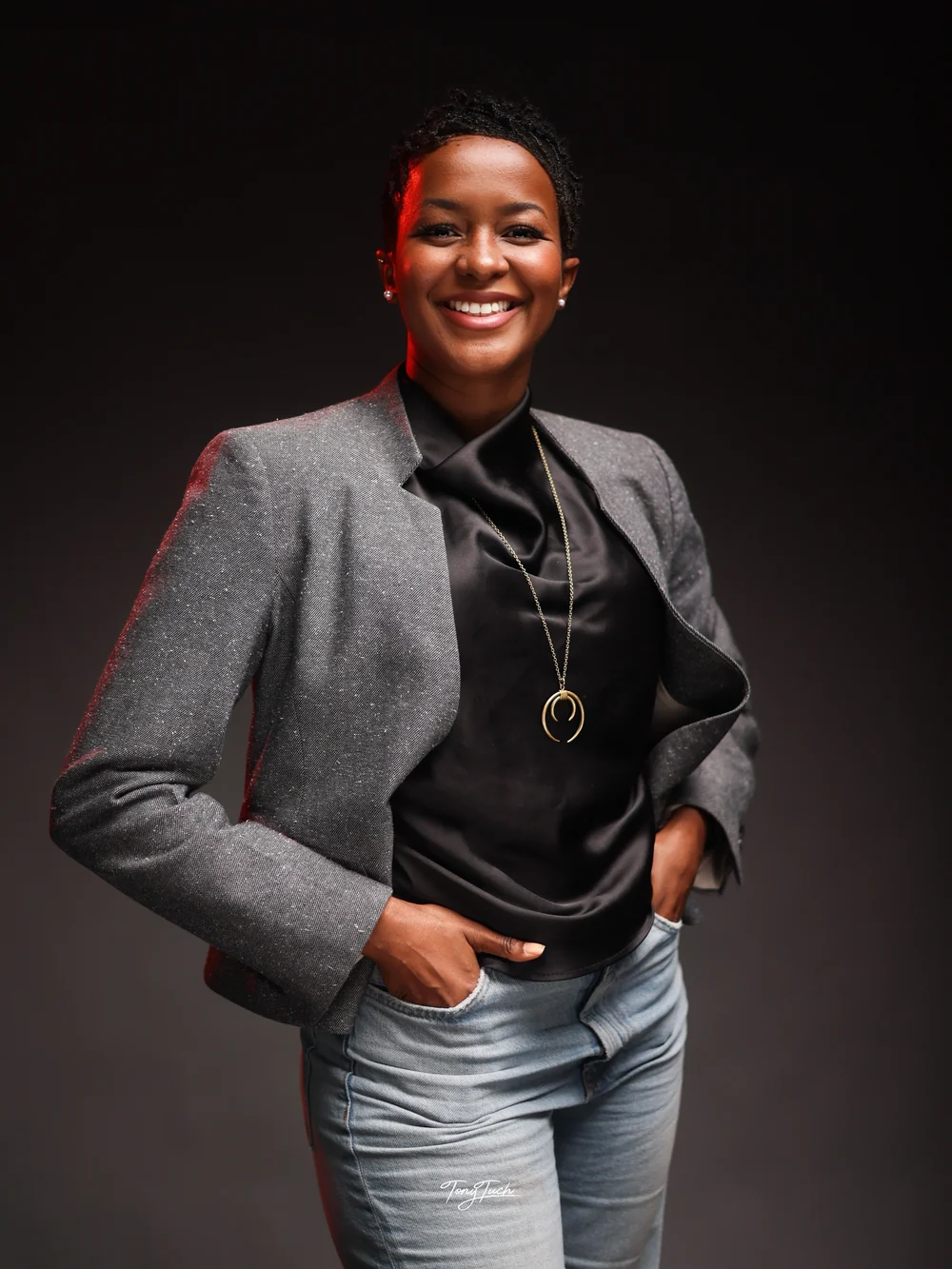 The coach smiling in a grey blazer and black blouse, with a relaxed, confident stance.