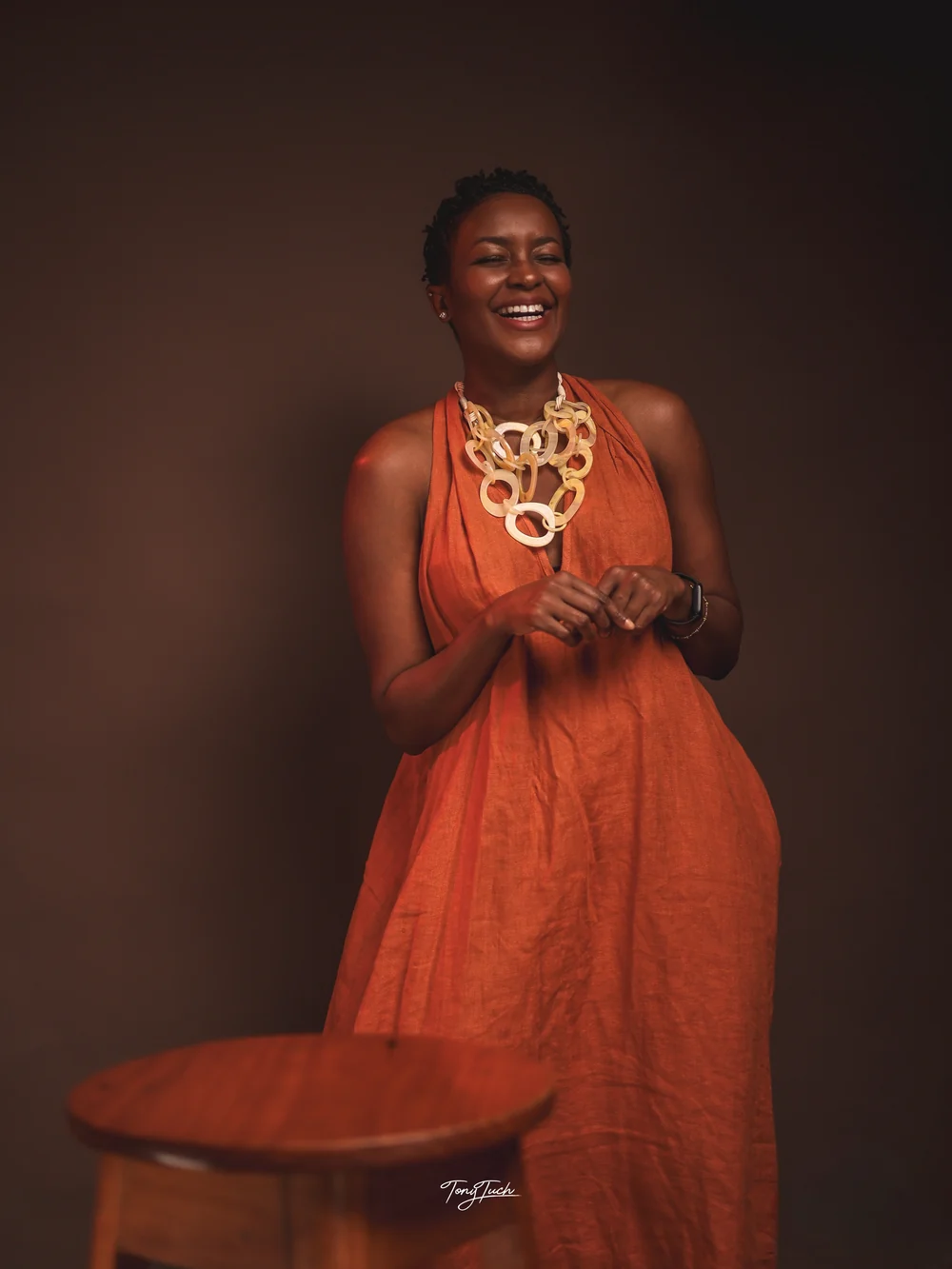 The coach laughing warmly in a flowing orange dress, with her hands gently resting together.